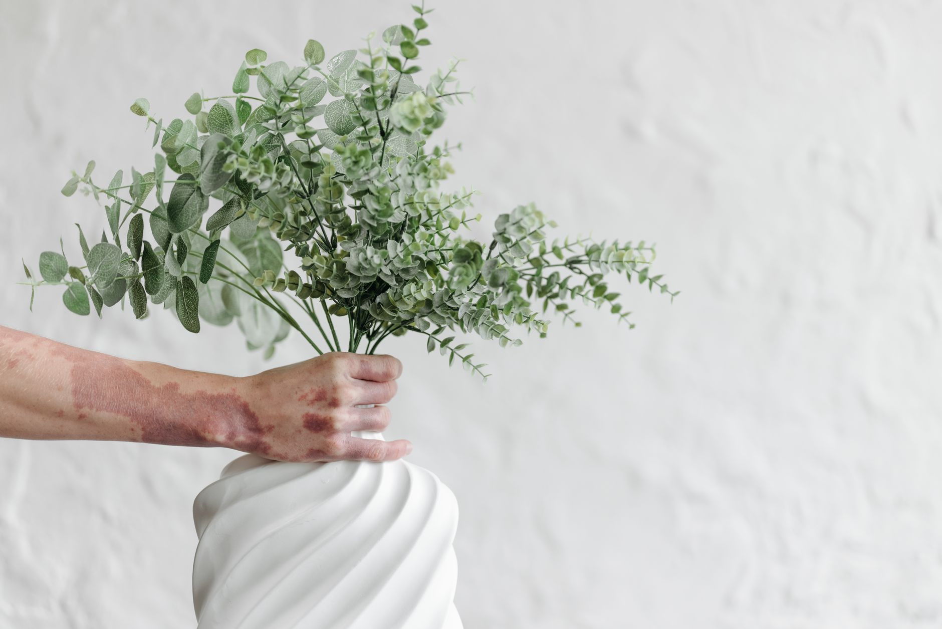 A vase of fresh eucalyptus on a bright desk
