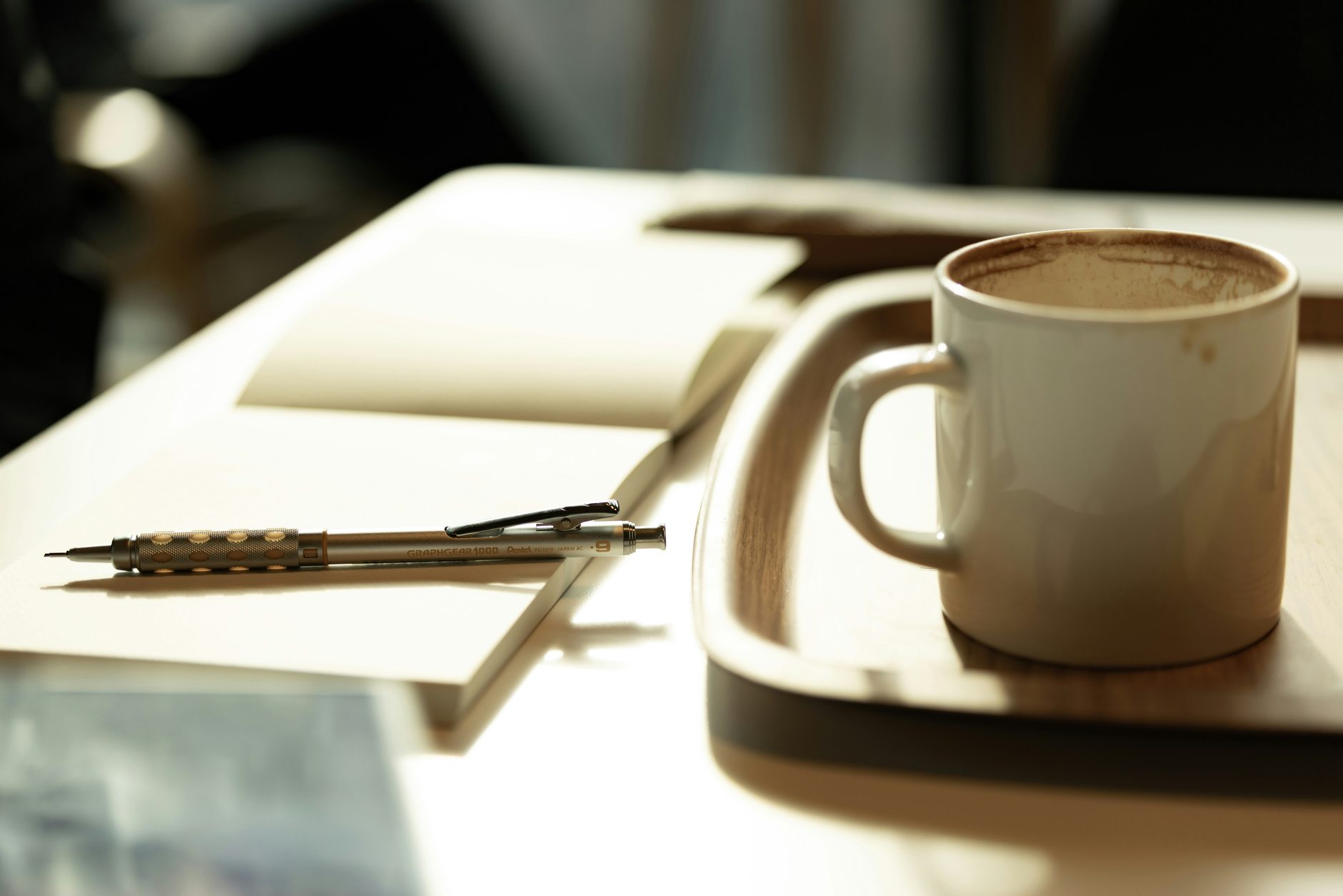 An open notebook, pencil and coffee on a sunlit desk